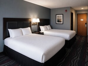 A hotel room with two beds, a nightstand with a lamp, a framed picture on the wall, and a door with a lock.