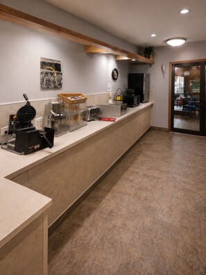 A clean, modern kitchen area with a long counter, a waffle maker, a coffee machine, and a microwave.