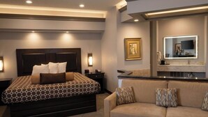 A bedroom with a large bed, a sofa, a vanity with a mirror, and a framed picture on the wall. - Apple Tree Inn and Suites (Independence)