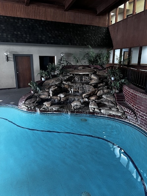 Relax by the tranquil pool surrounded by lush greenery and a natural rock feature.