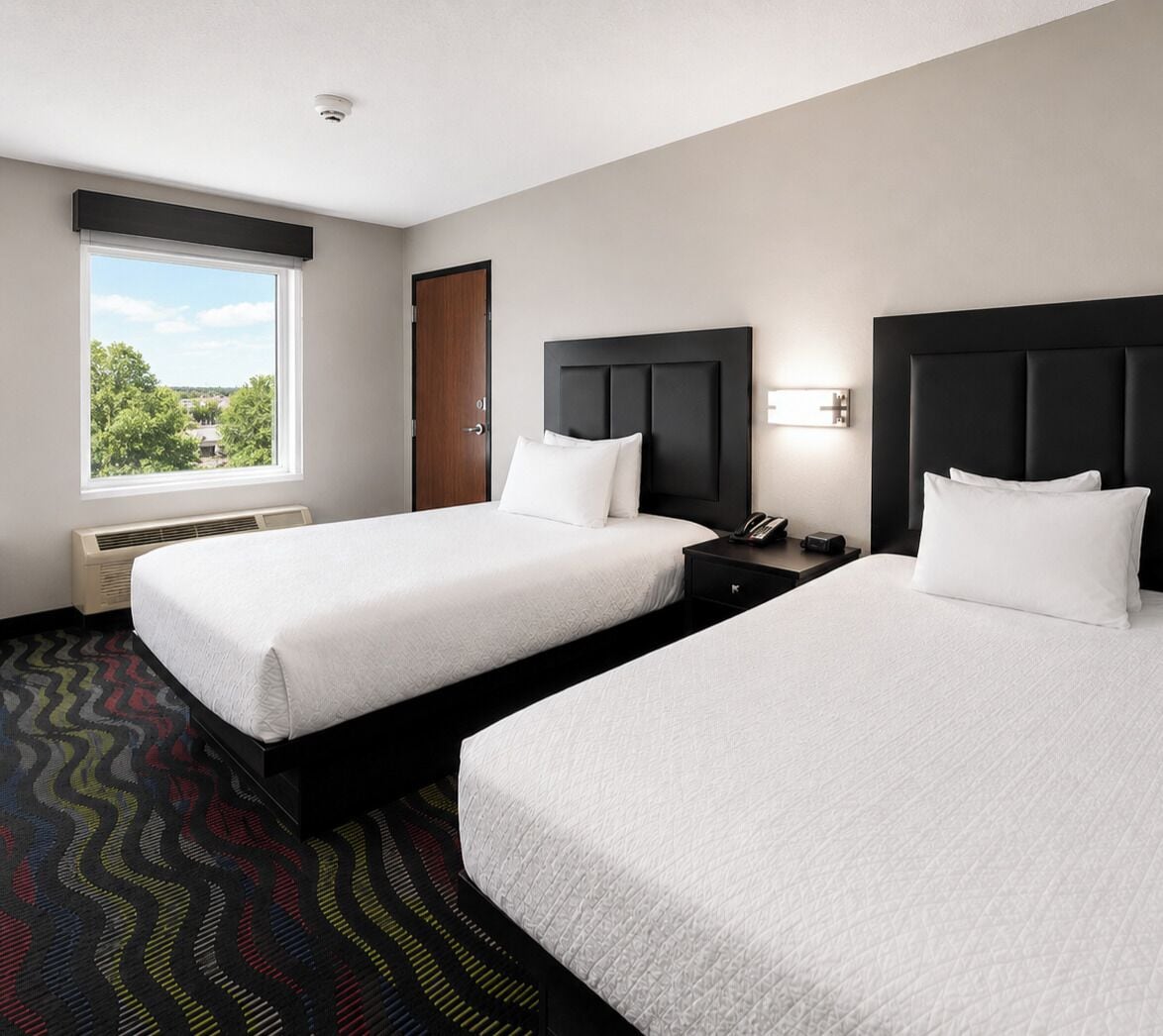 A hotel room with two beds, a window with a view, a door, and a nightstand with a phone.