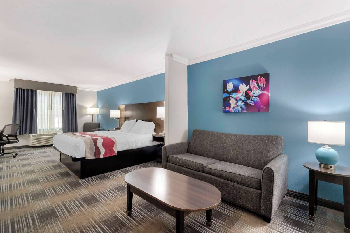 Una camera d'albergo con un letto, un divano, un tavolino da caffè e un quadro appeso al muro.