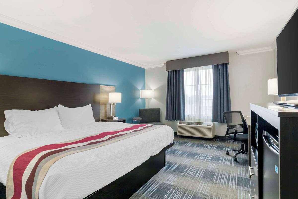 Una camera d'hotel con un letto grande, due abat-jour, una scrivania con un computer, un condizionatore d'aria e una finestra con tende.