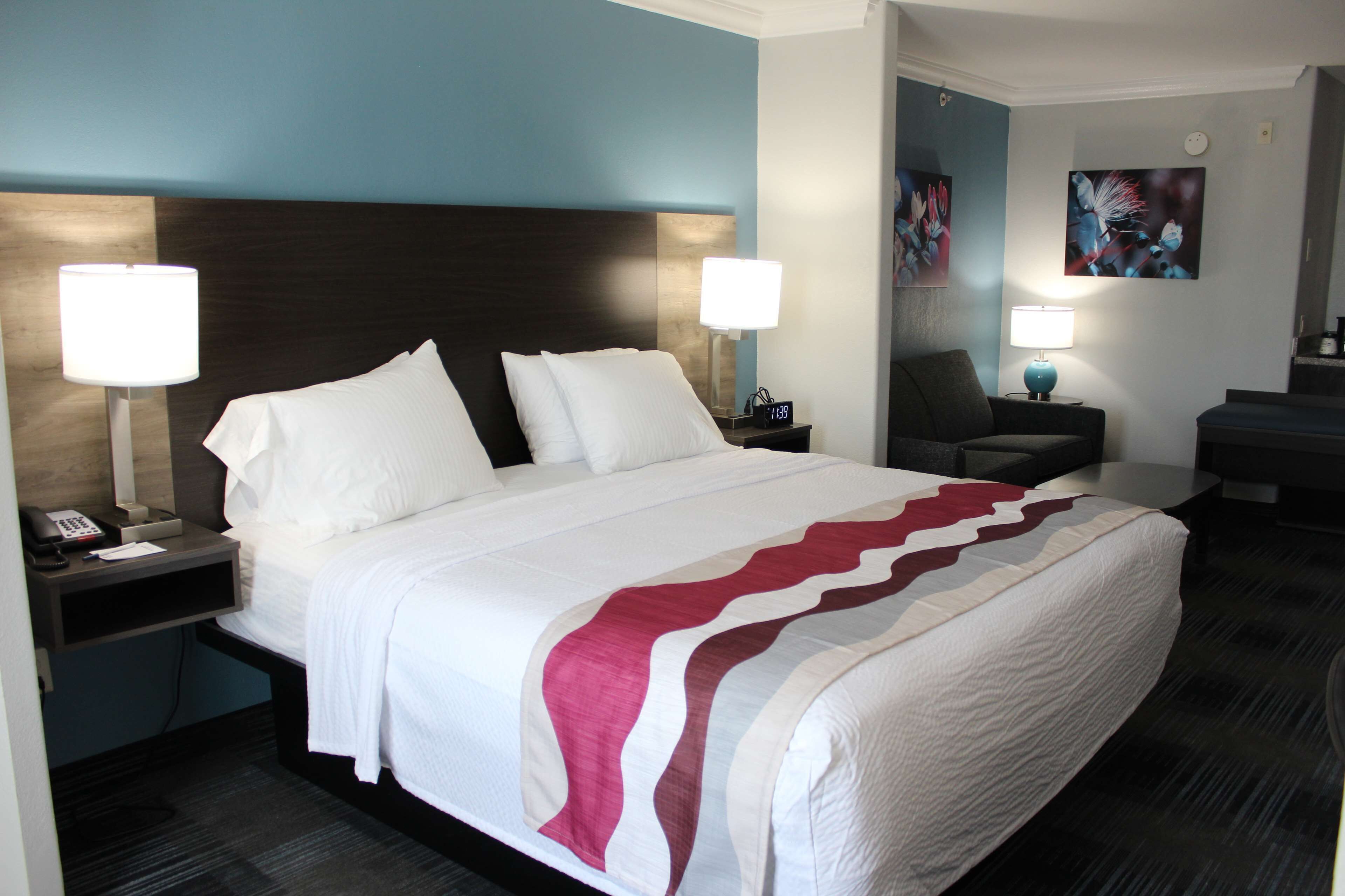 A hotel room with a large bed, two bedside tables with lamps, a chair, and artwork on the walls.