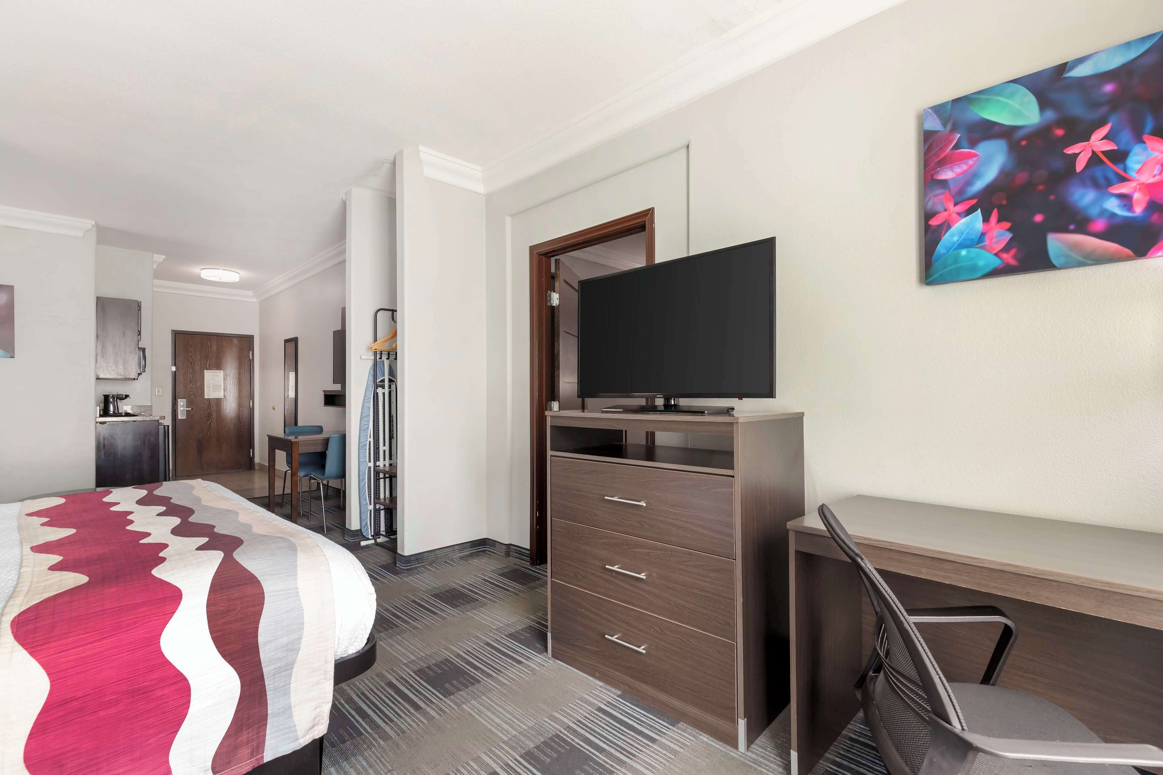A hotel room with a bed, a desk, a TV, and a painting on the wall.