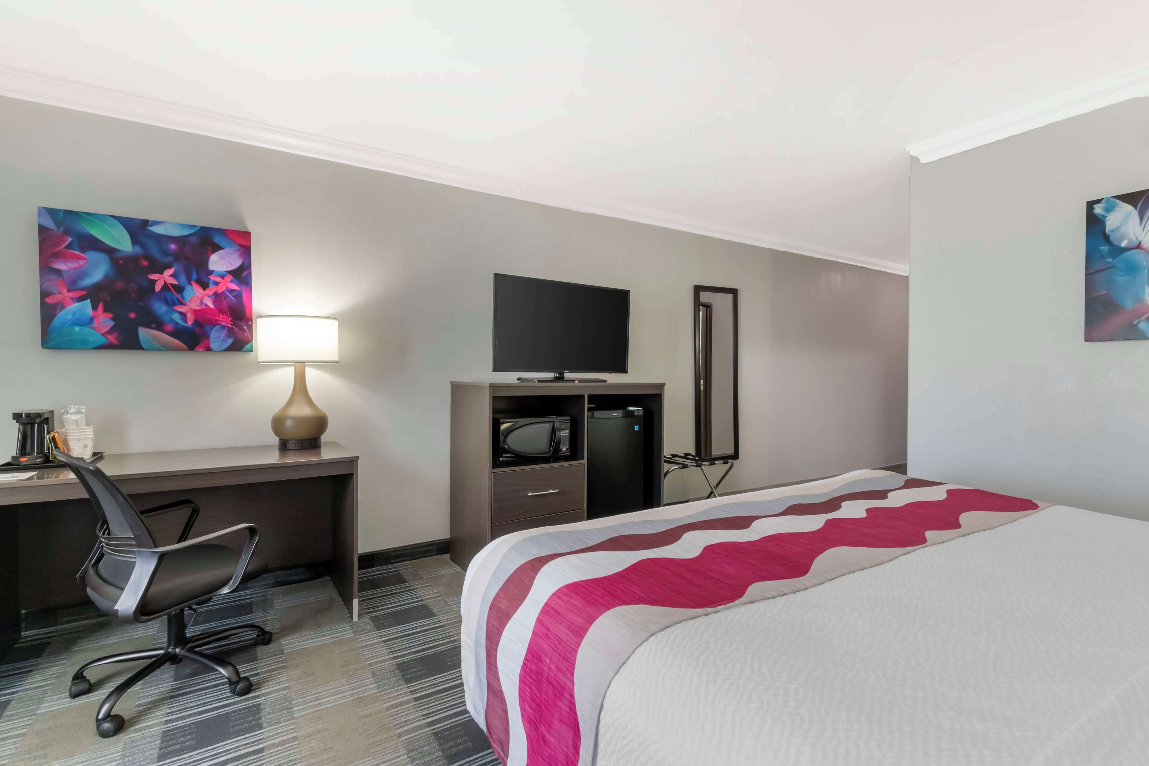 Een hotelkamer met een bed, een bureau met stoel, een televisie en kunstwerken aan de muur.