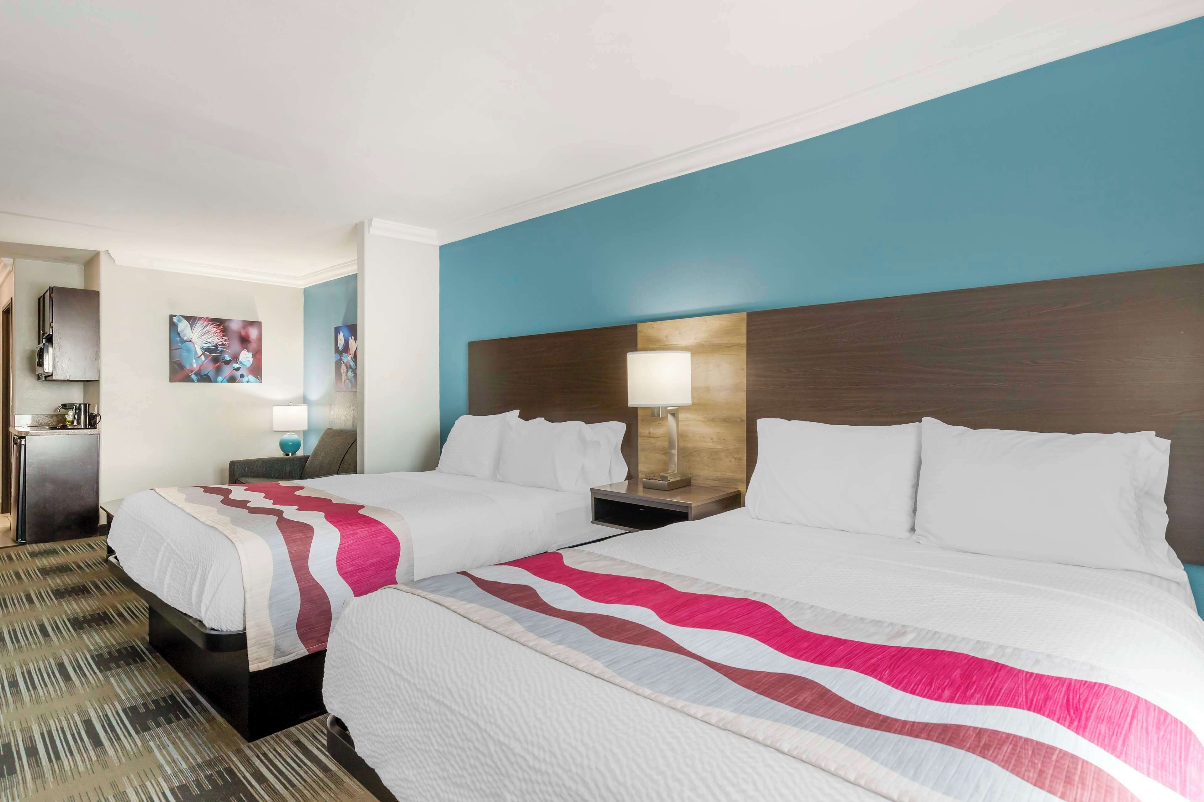 A hotel room with two beds, a wooden headboard, a nightstand with a lamp, and a painting on the wall.