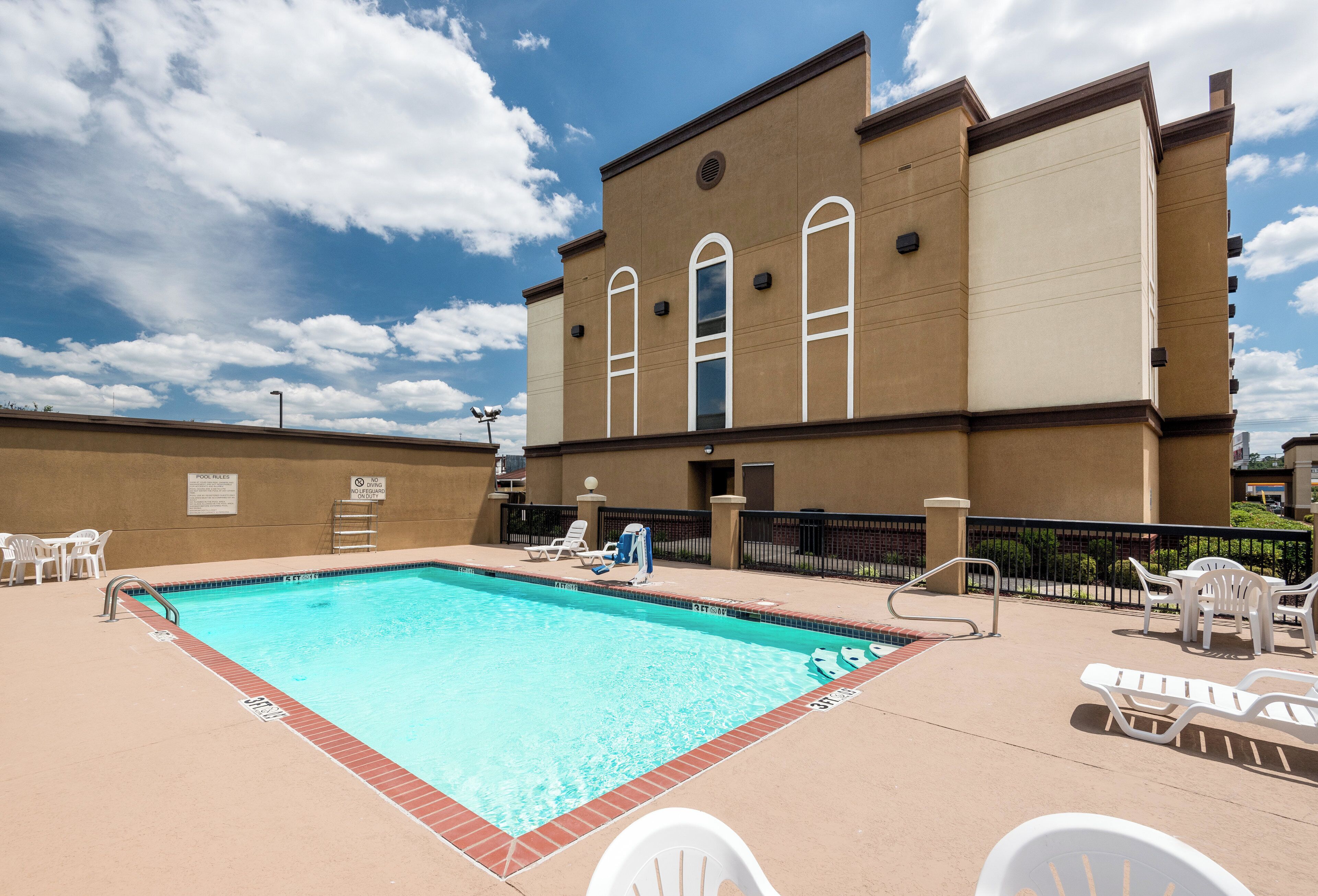 Una piscina con sillones de descanso y un edificio con ventanas de arco en el fondo.