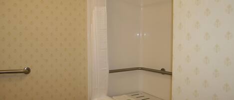 A bathroom with patterned wallpaper, a shower curtain, a towel rack, and a shelf with a towel.