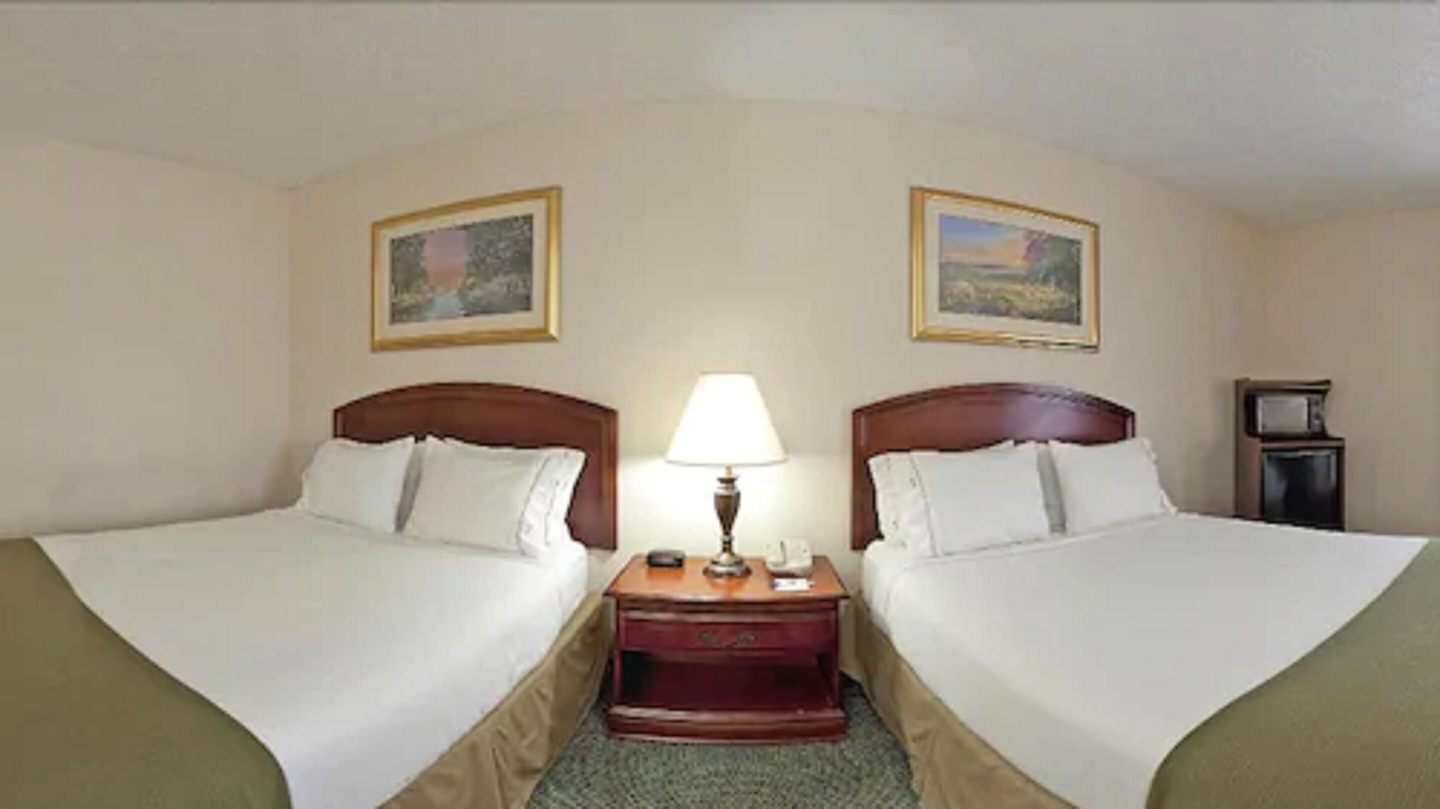 Une chambre d’hôtel avec deux lits, une table de chevet avec une lampe, une petite table et un téléviseur.