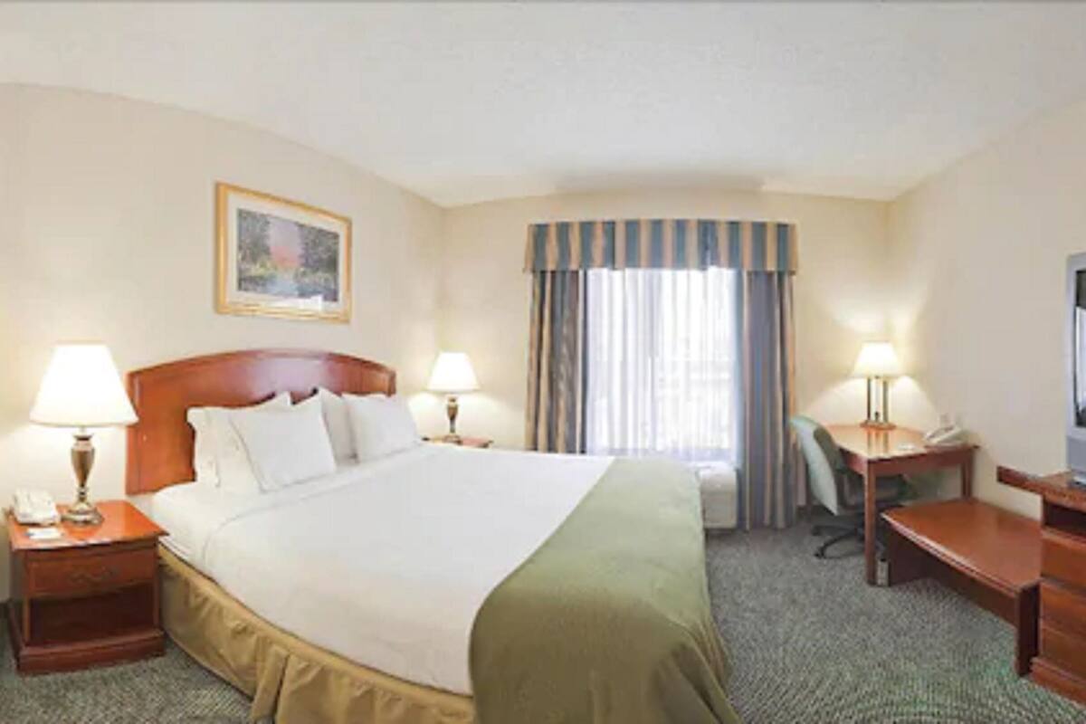 A hotel room with a large bed, two bedside tables with lamps, a desk, and a chair.