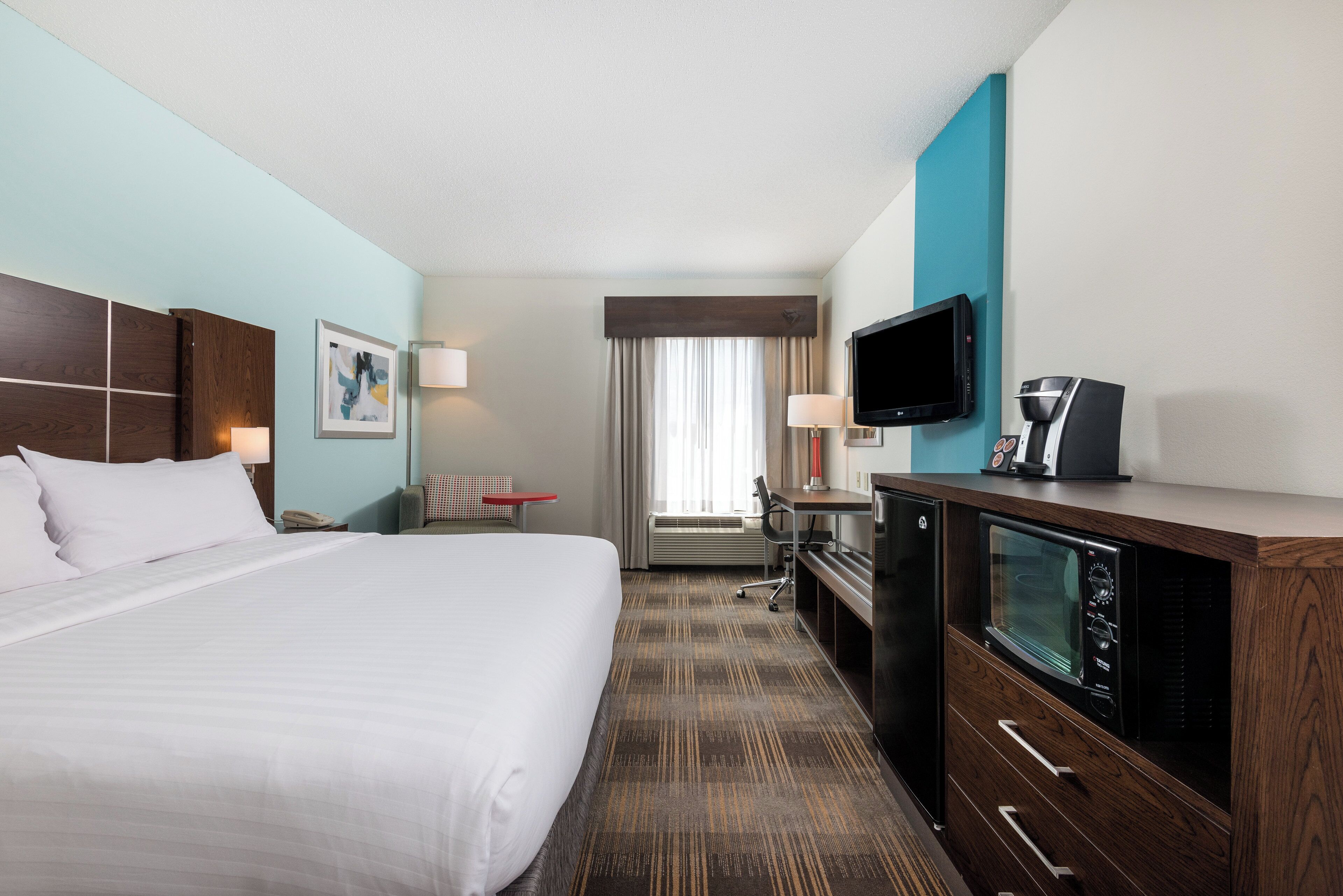 A hotel room with a large bed, a desk with a computer, a television, and a coffee maker.