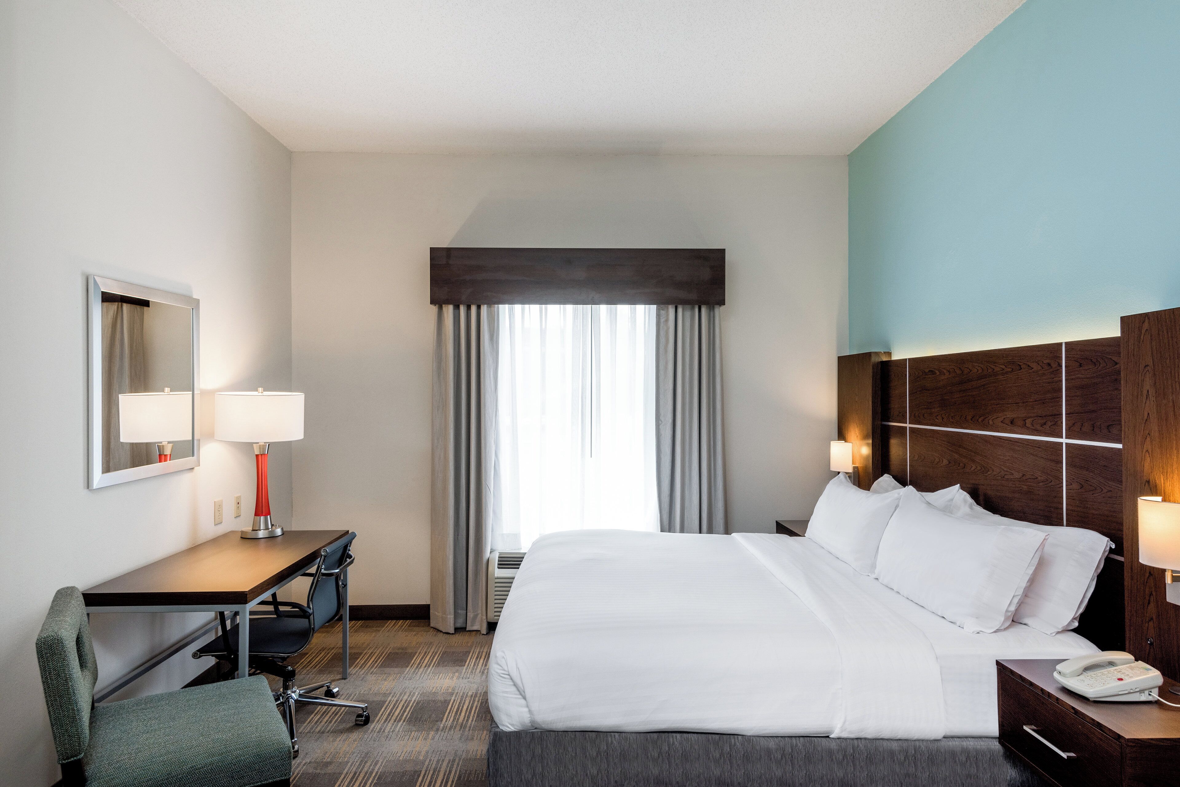 Une chambre d’hôtel avec un lit, un bureau, une chaise et une grande fenêtre avec des rideaux.