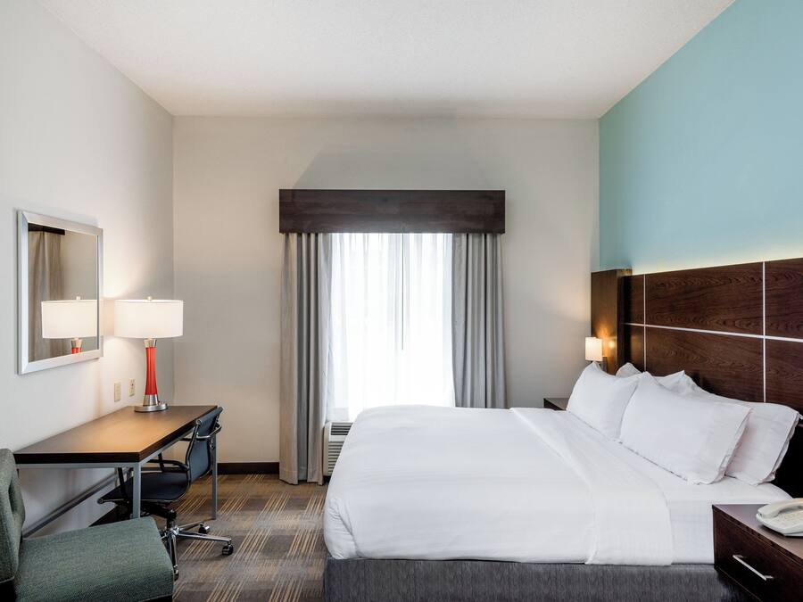 Une chambre d’hôtel avec un lit, un bureau, une chaise et une grande fenêtre avec des rideaux.