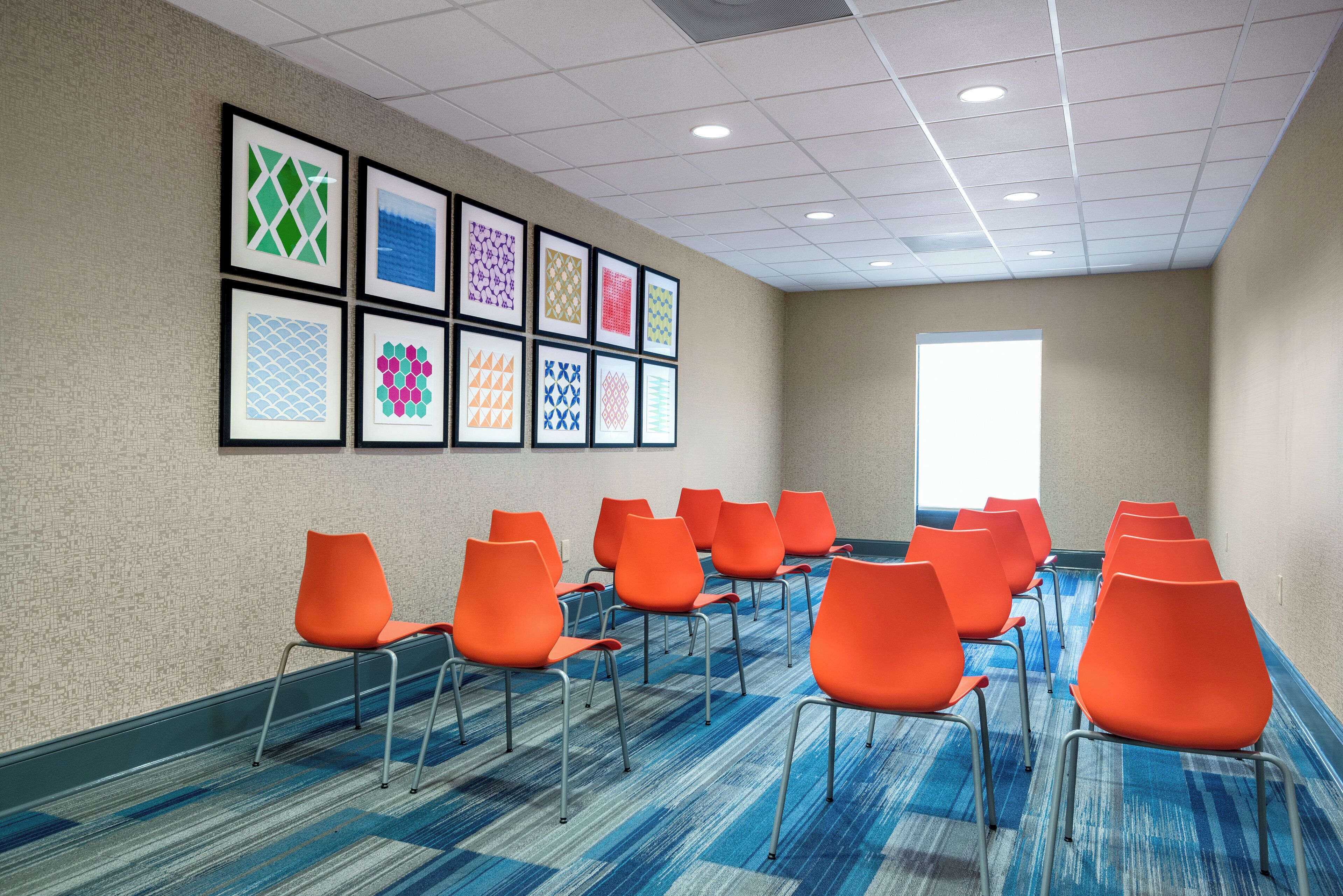 A conference room with a row of orange chairs, a patterned carpet, and framed artwork on the wall.