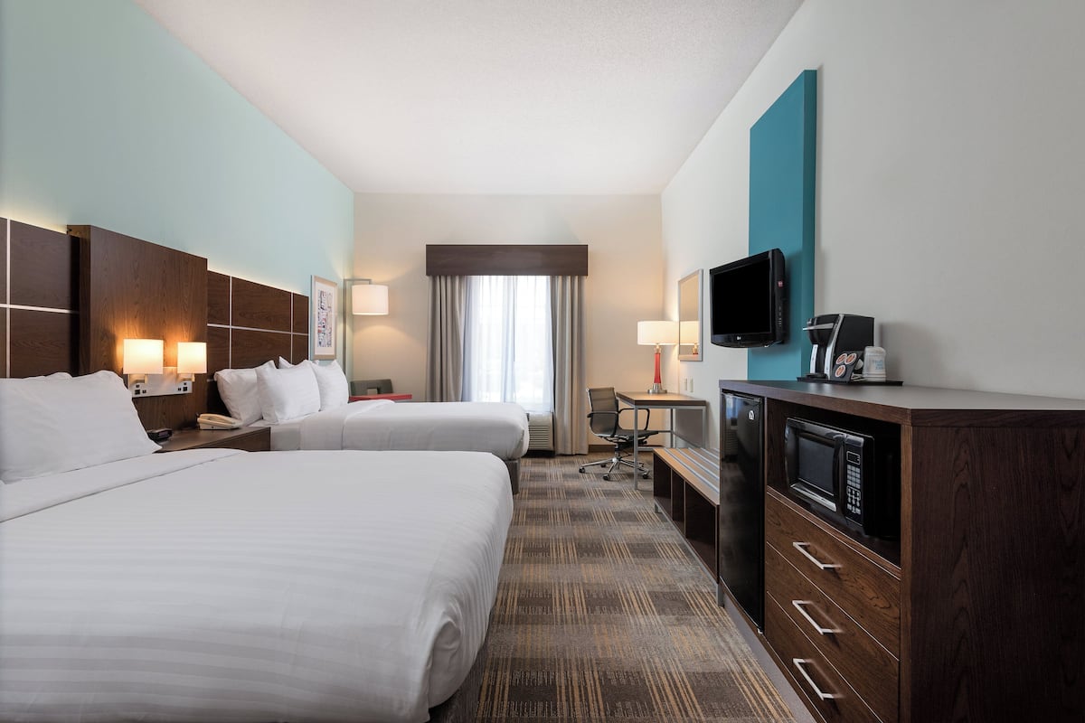 A hotel room with two beds, a desk with a computer, a TV, and a microwave.