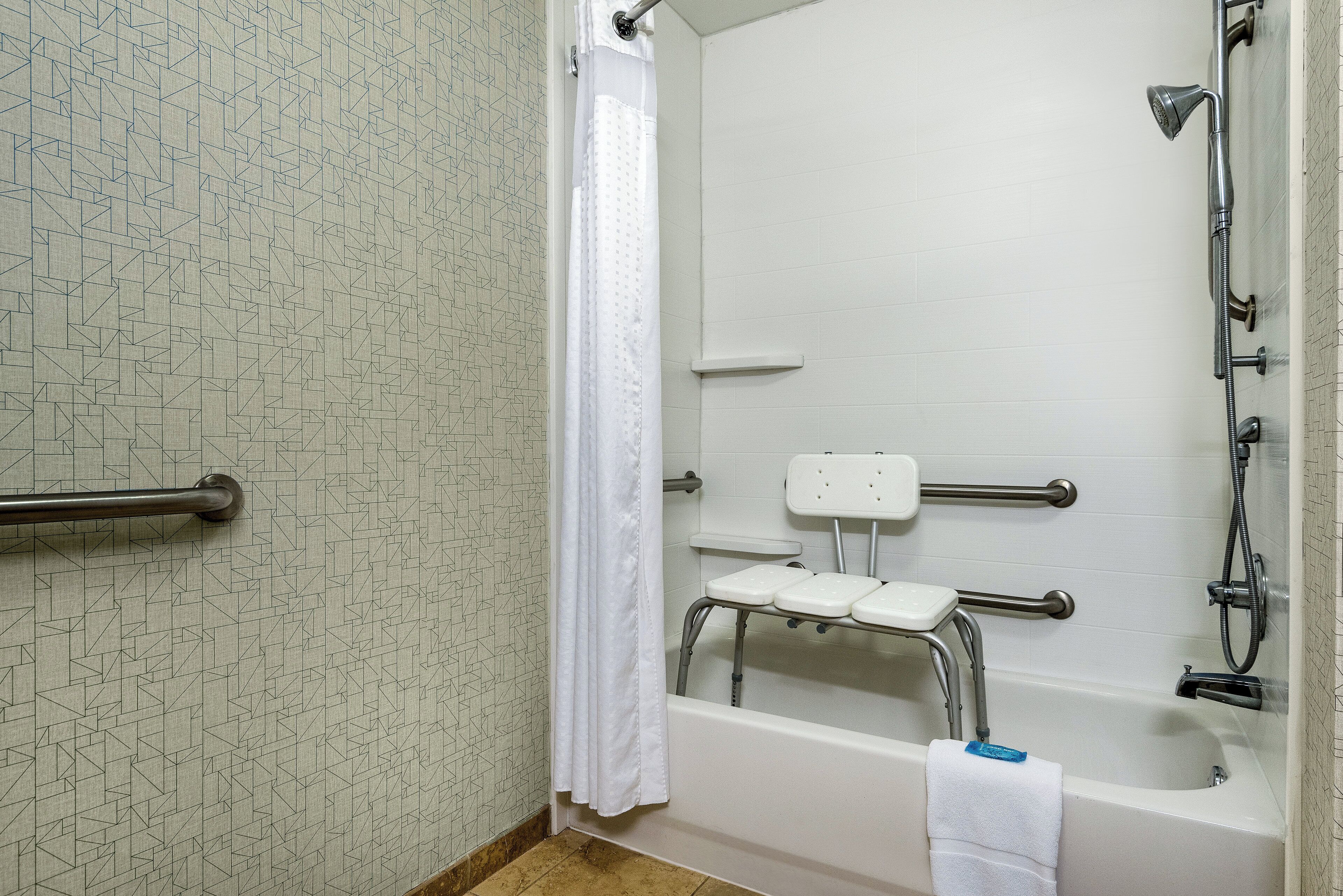 A bathroom with a shower, grab bars, a step stool, and a towel rack.