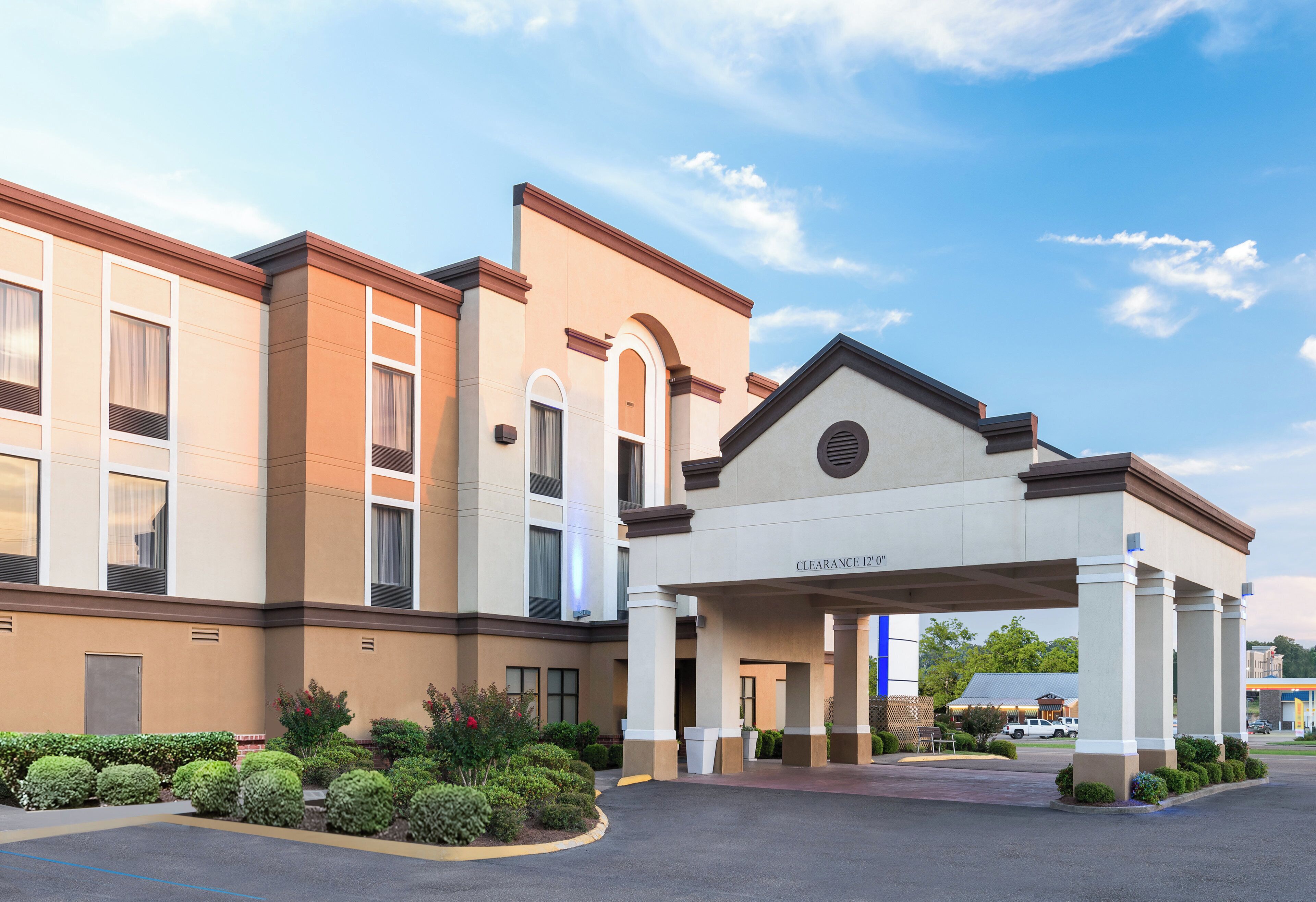 A hotel entrance with a covered walkway, a clear sky, and a parking lot.