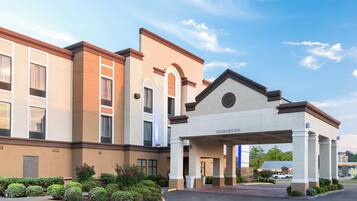 A hotel entrance with a covered walkway, a clear sky, and a parking lot.