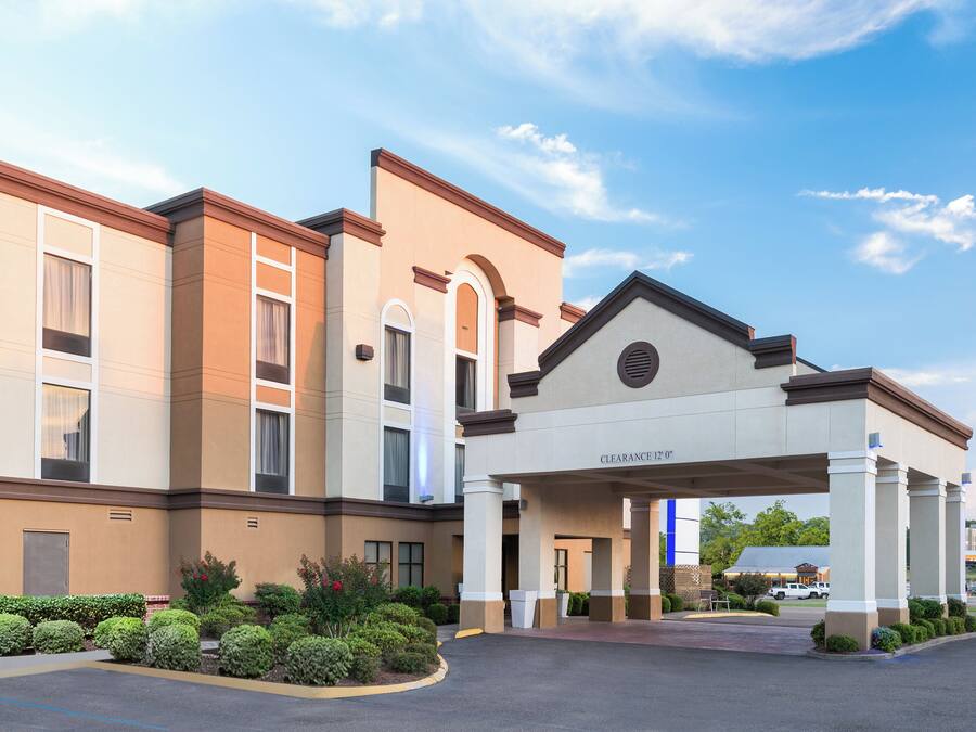 A hotel entrance with a covered walkway, a clear sky, and a parking lot.