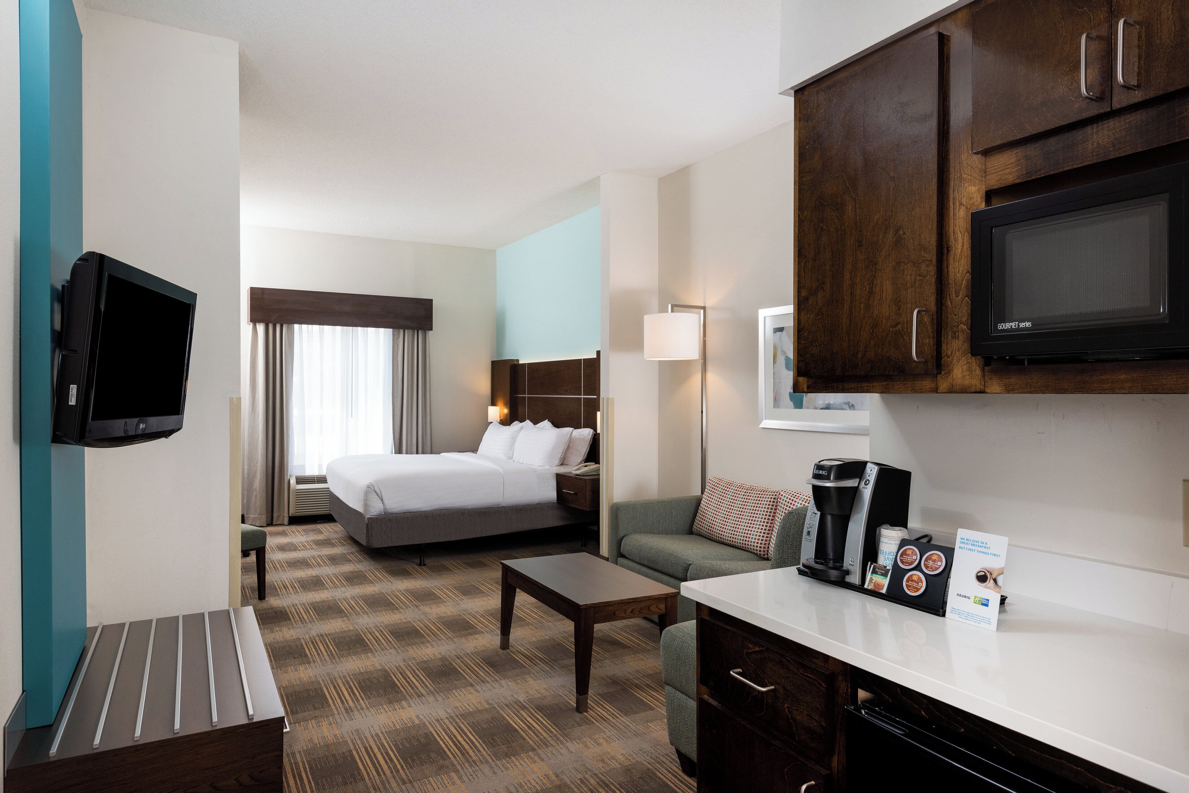 A hotel room with a bed, a desk, a microwave, a coffee maker, and a television.
