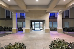 Una entrada de edificio con una puerta central, flanqueada por columnas y un suelo de baldosas.