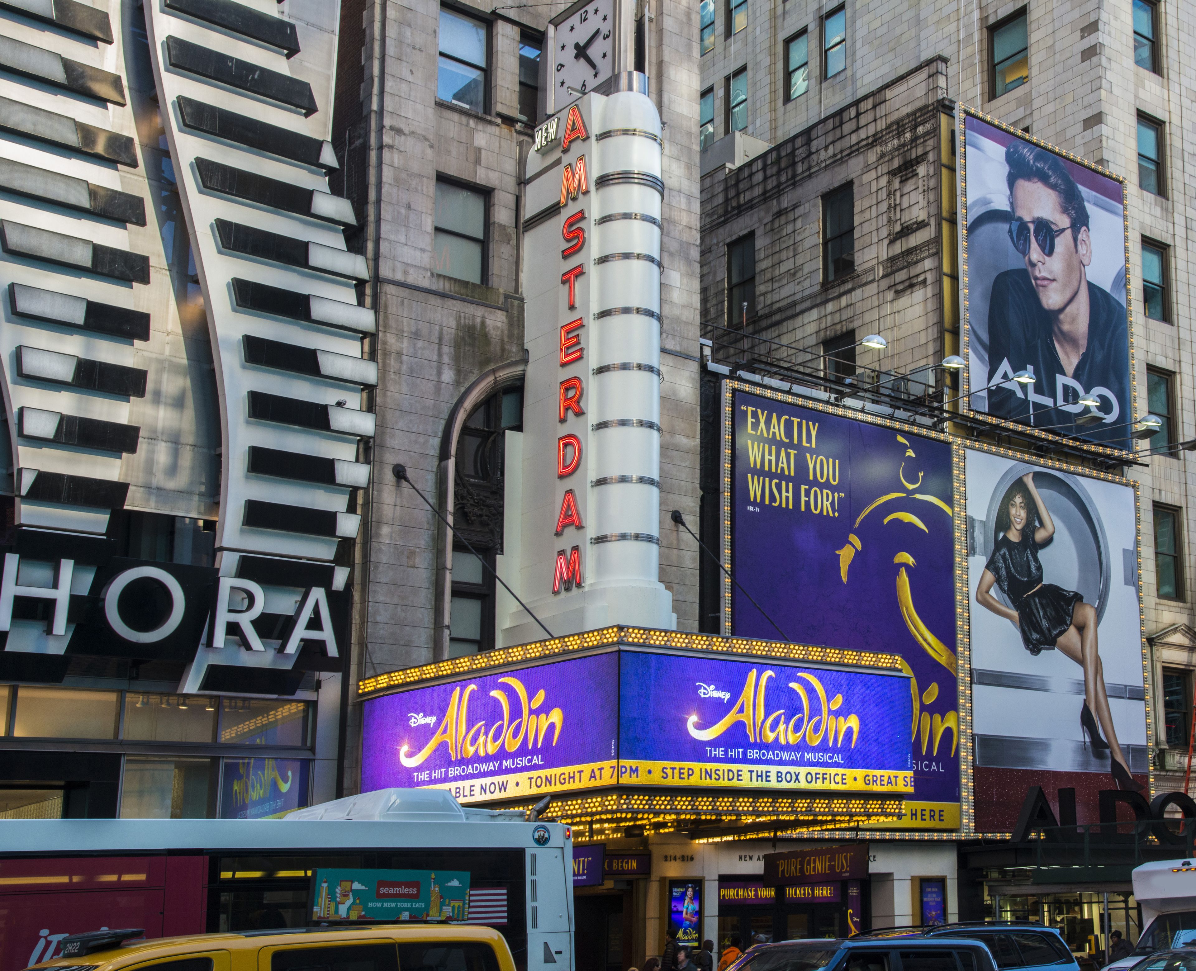 A theater with a marquee advertising 'Aladdin' and a clock above the entrance.