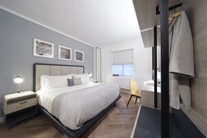 Un dormitorio moderno con cama, mesitas de noche, una silla y una obra de arte en la pared.
