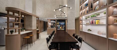 Un comedor moderno y bien iluminado con una mesa larga, taburetes de bar y estantes con libros y objetos decorativos.