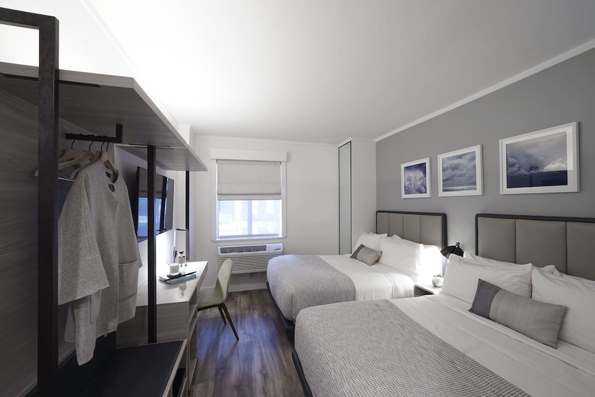 A modern hotel room with two beds, a desk, and a walk-in closet.