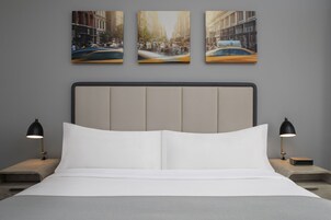 Een moderne hotelkamer met een groot bed, twee nachtkastjes en drie ingelijste stadsgezichten aan de muur.
