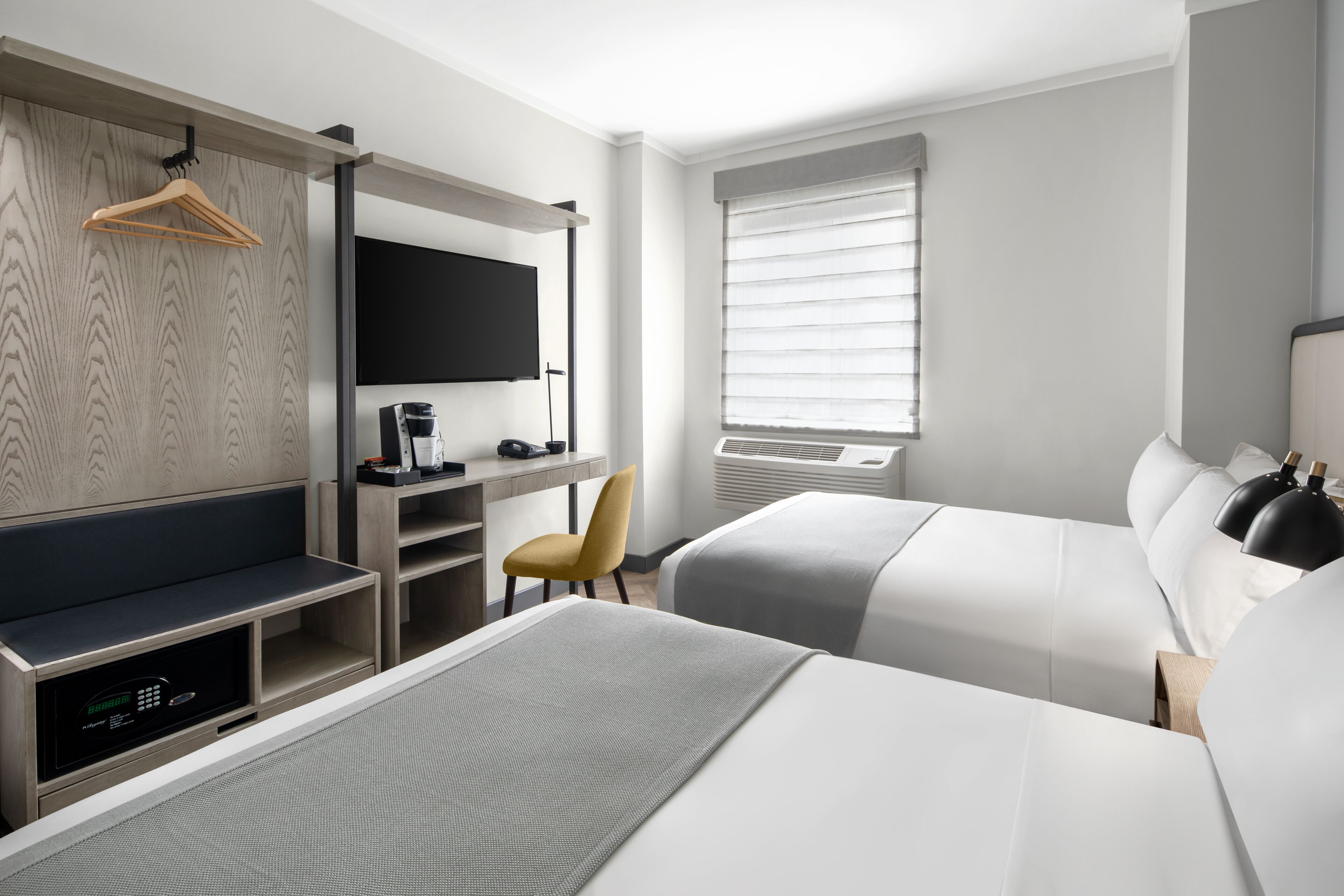Een moderne hotelkamer met twee bedden, een televisie, een koffieapparaat en een bureau.