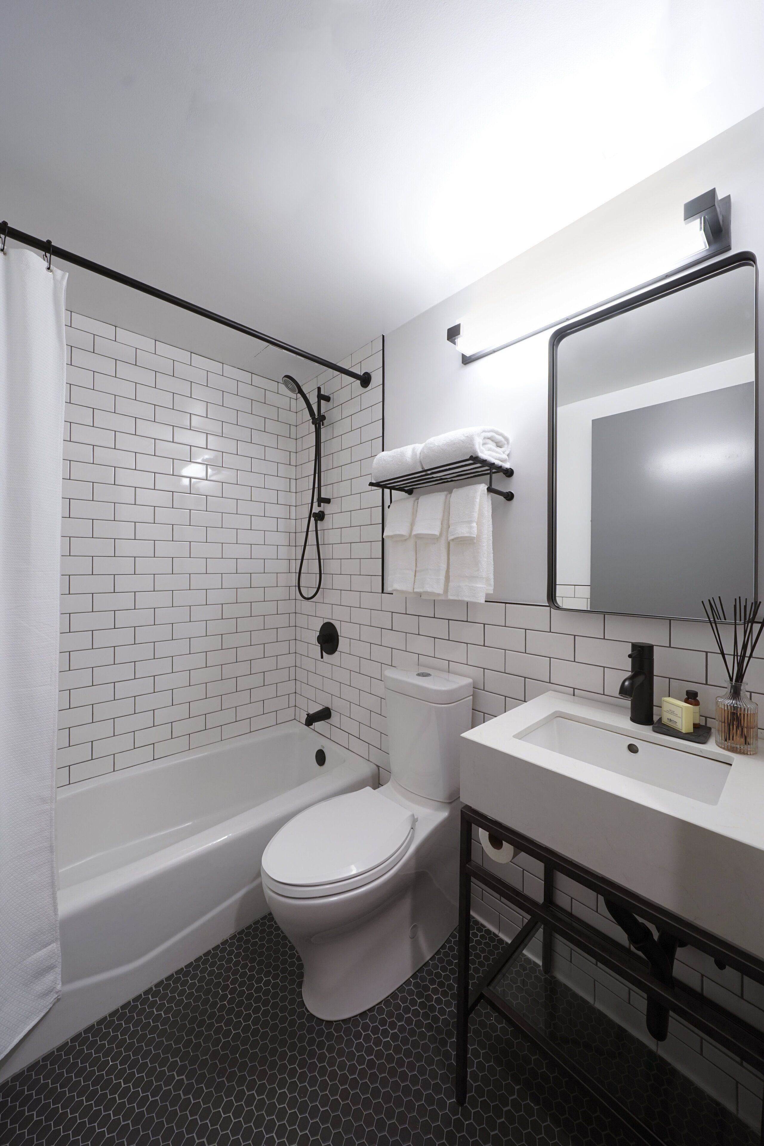 A bathroom with white subway tiles, a white toilet, a white bathtub, and a white sink with a mirror above it.