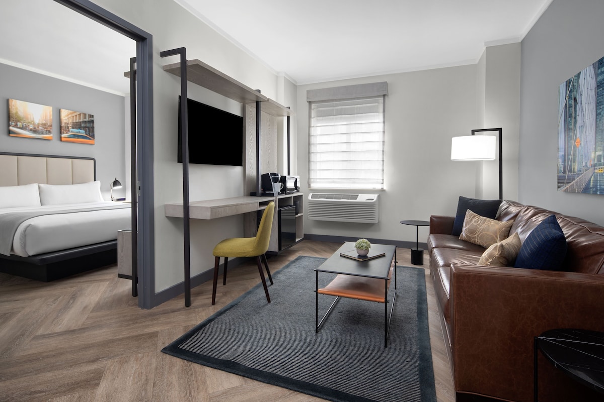 Een moderne hotelkamer met een bed, een bureau met stoel, een bank en een aan de muur bevestigde televisie.