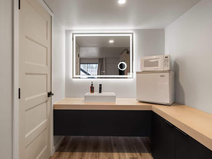 A modern kitchen with a built-in microwave, a sink with a mirror above it, and a wooden countertop.