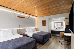 Una habitación de hotel moderna con dos camas, un escritorio, una silla, un ventanal y techo de madera.