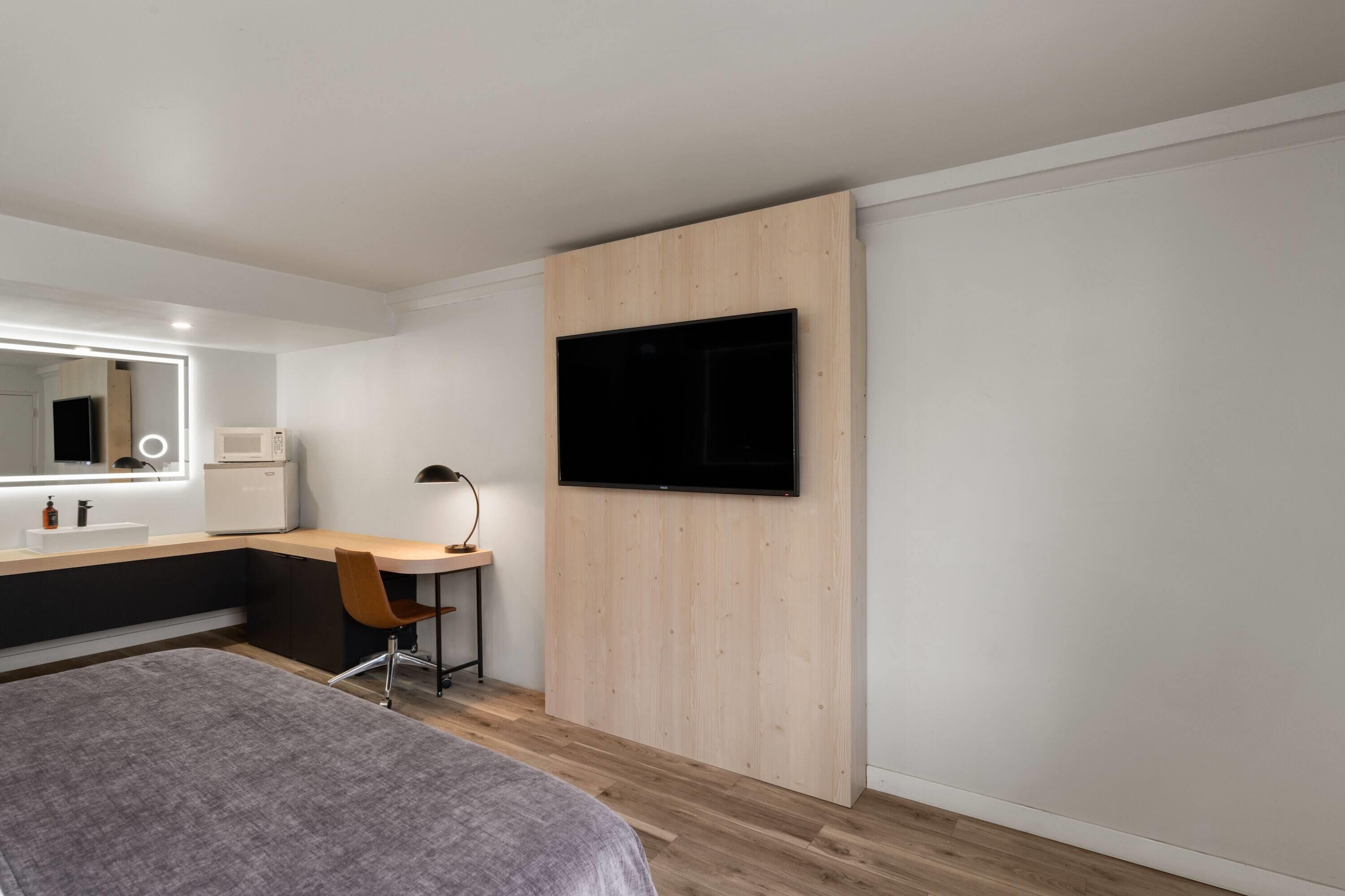 A modern bedroom with a bed, a desk, a chair, a TV, and a large mirror.