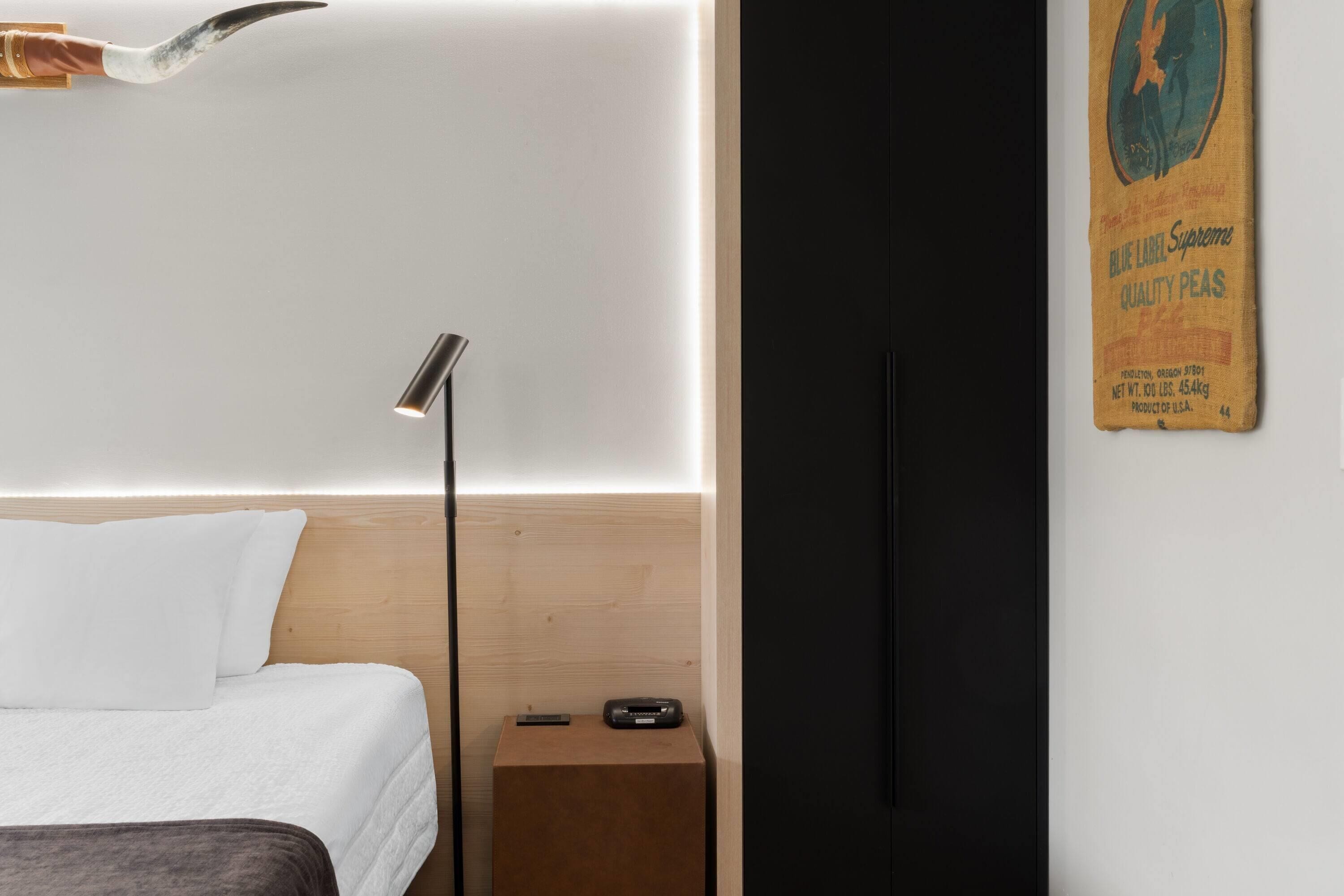 Una habitación de hotel moderna con cama, mesita de noche, lámpara y un cartel en la pared.
