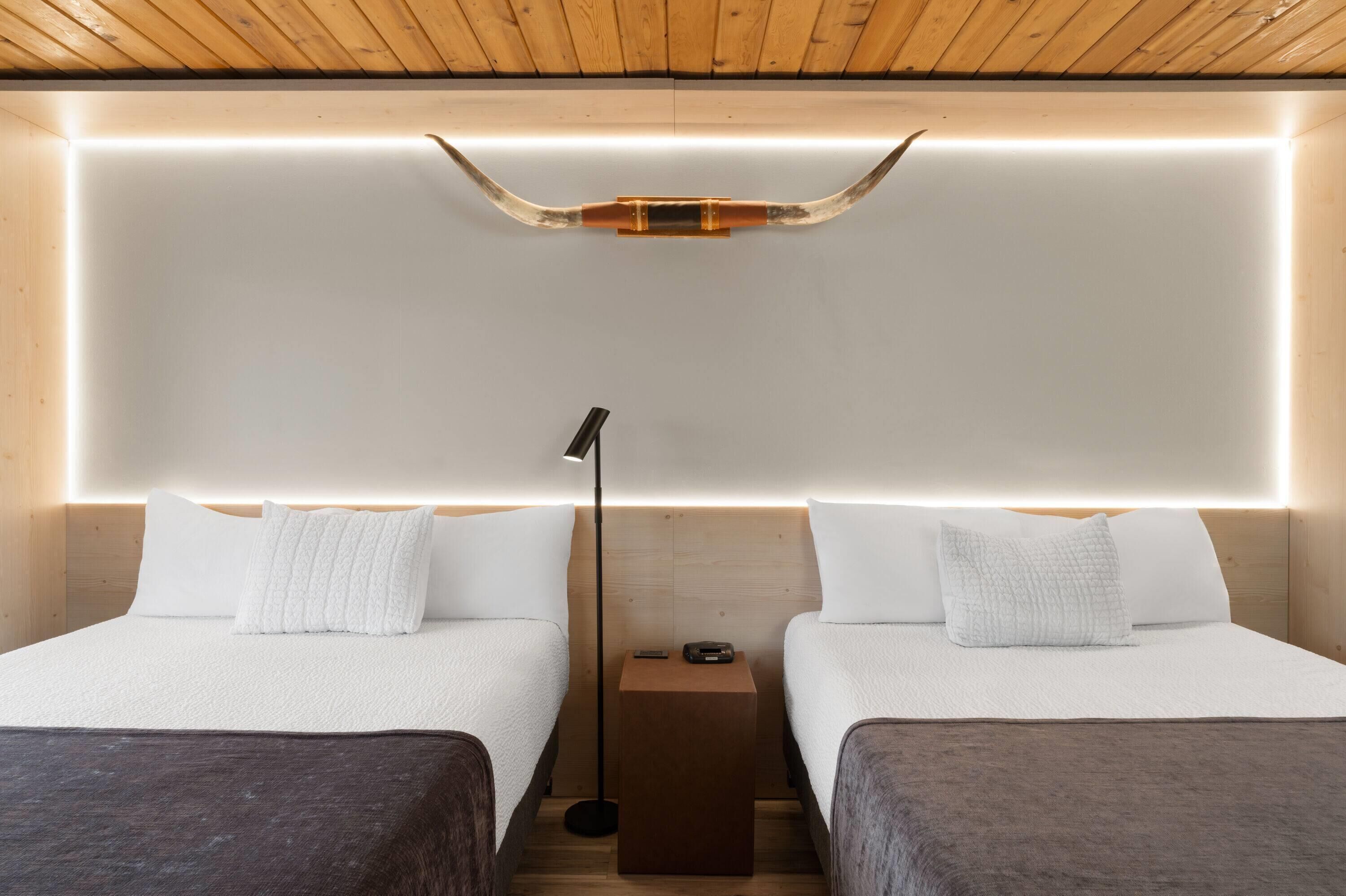 Ein modernes Hotelzimmer mit zwei Betten, einem Nachttisch, einer Lampe und einer auffälligen Deckenleuchte.