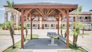 Un espacio de estar al aire libre cubierto con un banco, palmeras y un edificio al fondo.