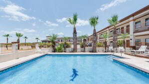 Piscina con sillones de descanso y palmeras, rodeada por un edificio con balcones.