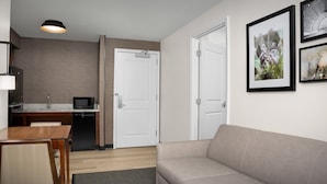 A modern living room with a sofa, a dining table with chairs, a kitchen area with a microwave, and a door. - Residence Inn Houston West-Energy Corridor (Houston)