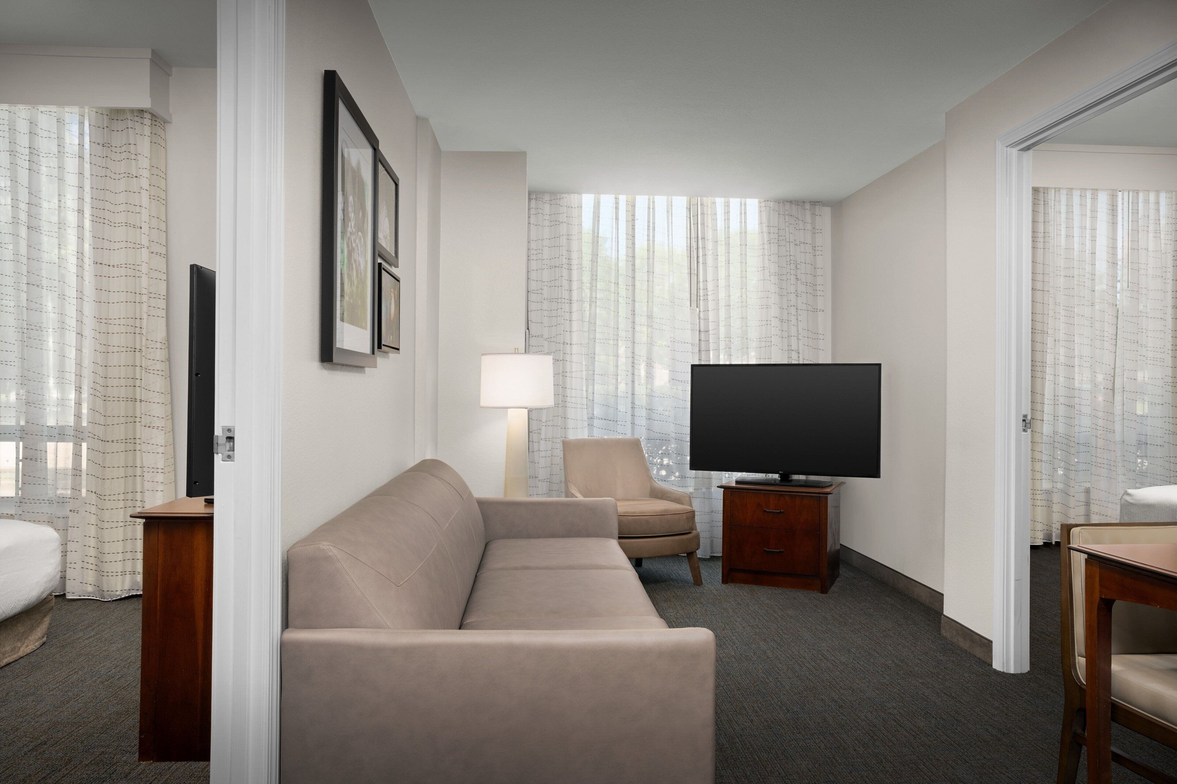 A hotel room with a sofa, a chair, a TV, a lamp, and a bed.
