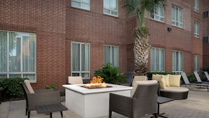 An outdoor patio with a fire feature, seating, and a brick building in the background. - Residence Inn Houston West-Energy Corridor (Houston)