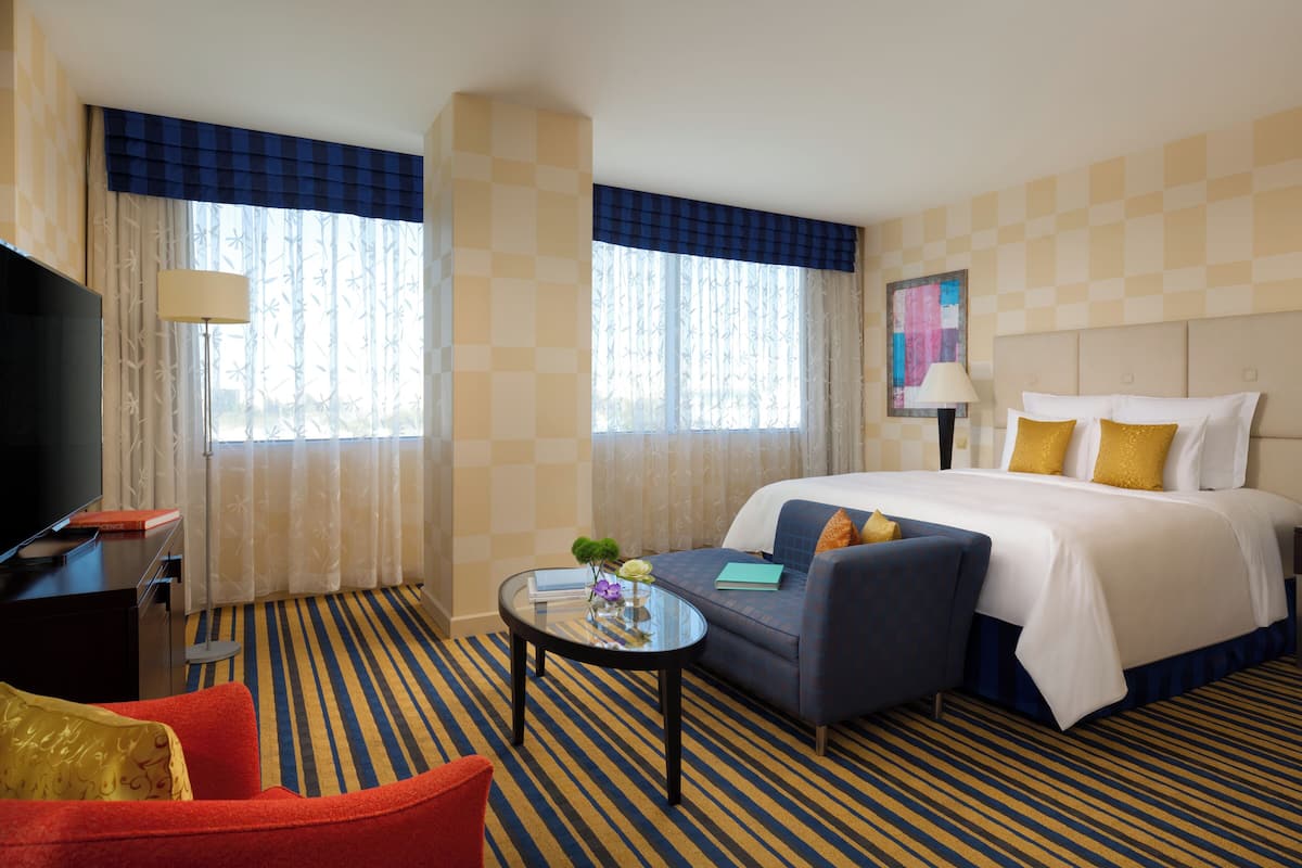 Ein Hotelzimmer mit einem Bett, einem Sofa, einem Fernseher, einem Schreibtisch und einem Vorhangfenster.