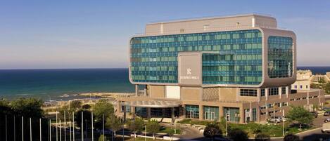 Un edificio moderno con fachada de vidrio, un llamativo logo 'R' y vista al mar.