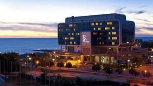 A modern hotel with a prominent 'R' logo, featuring a unique architectural design with multiple levels and a waterfront view. - Renaissance by Sulo (Aktau)