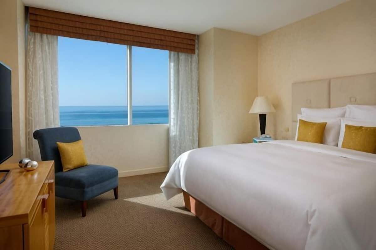 Ein Hotelzimmer mit Bett, Stuhl, Schreibtisch, Lampe und Meerblick.