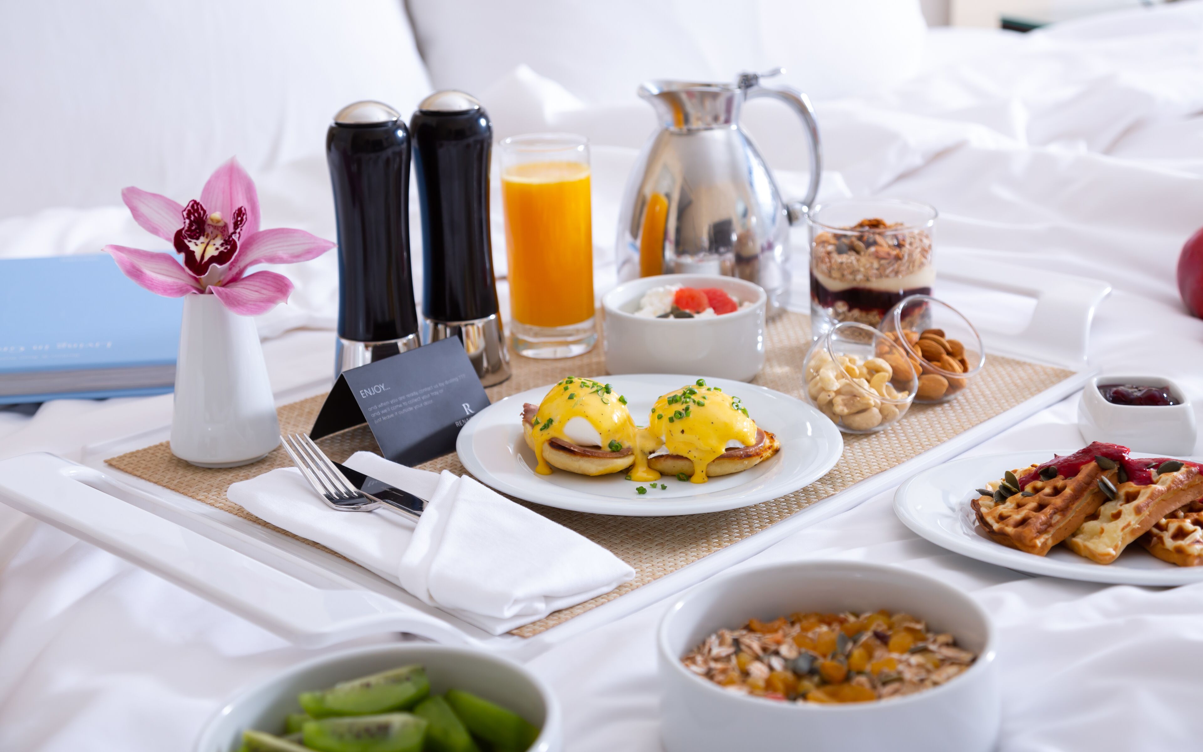 Ein Frühstückstisch im Bett mit Eggs Benedict, Waffeln und verschiedenen Speisen.