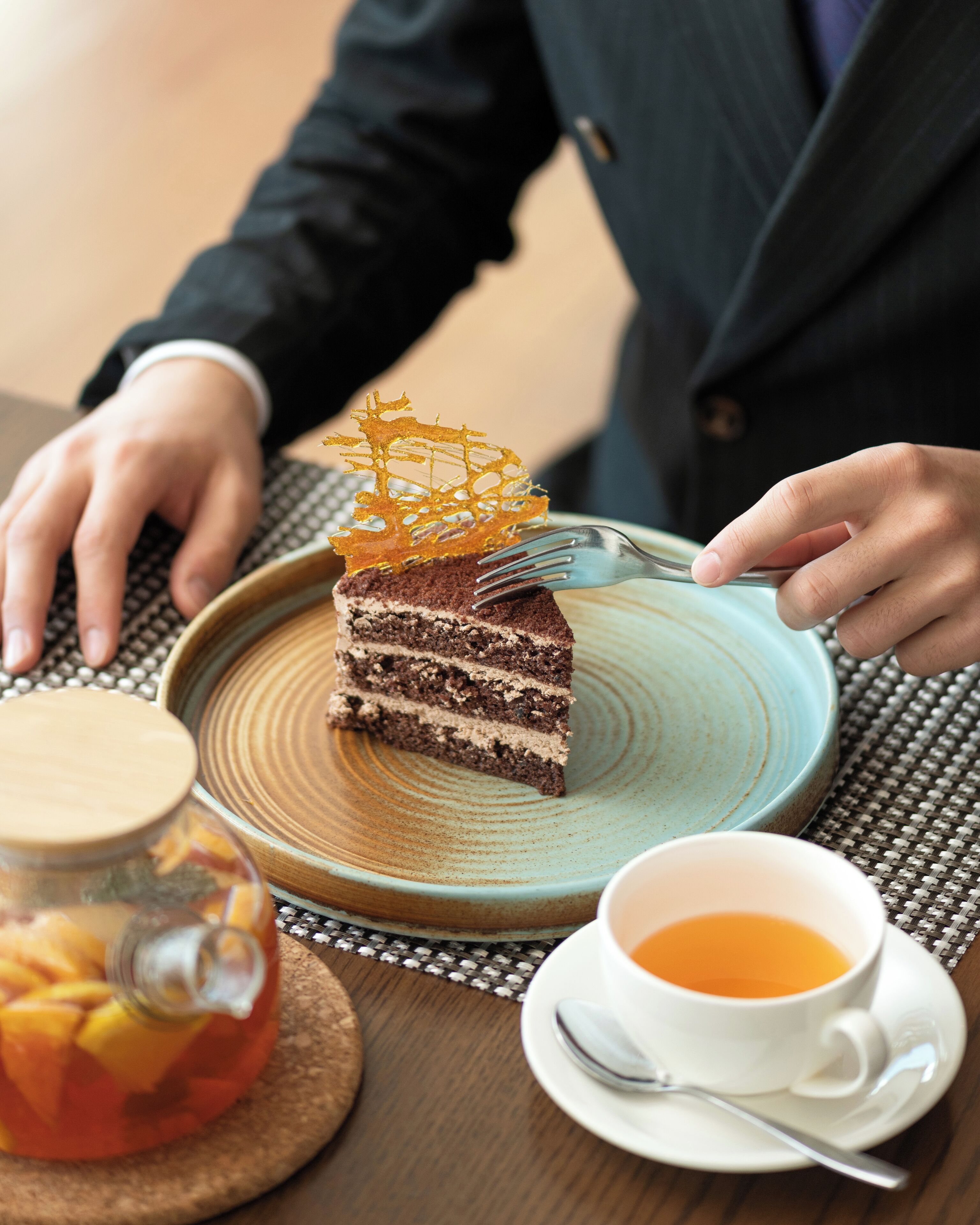 A slice of cake with a decorative topping on a plate, a cup of tea, and a glass jar with a lid.